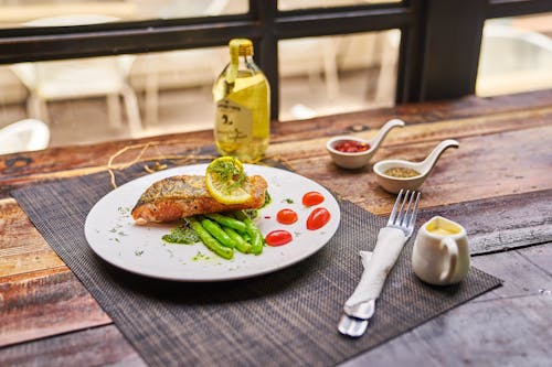 High angle of served plate with fried fish and vegetables placed near saucers with spices and olive oil