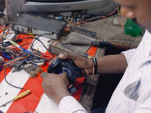 Free A focused technician repairing an electronic device amidst a cluttered workbench filled with tools and cables. Stock Photo
