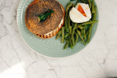 Free Ceramic plate with tasty fresh bagel and asparagus with poached egg served on white marble table in light modern kitchen at home Stock Photo