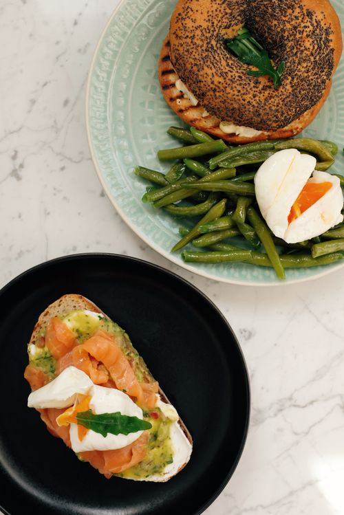 Free From above of crunchy bagel with poached egg and asparagus and plate of toast with salmon served on white marble table in modern kitchen at home Stock Photo