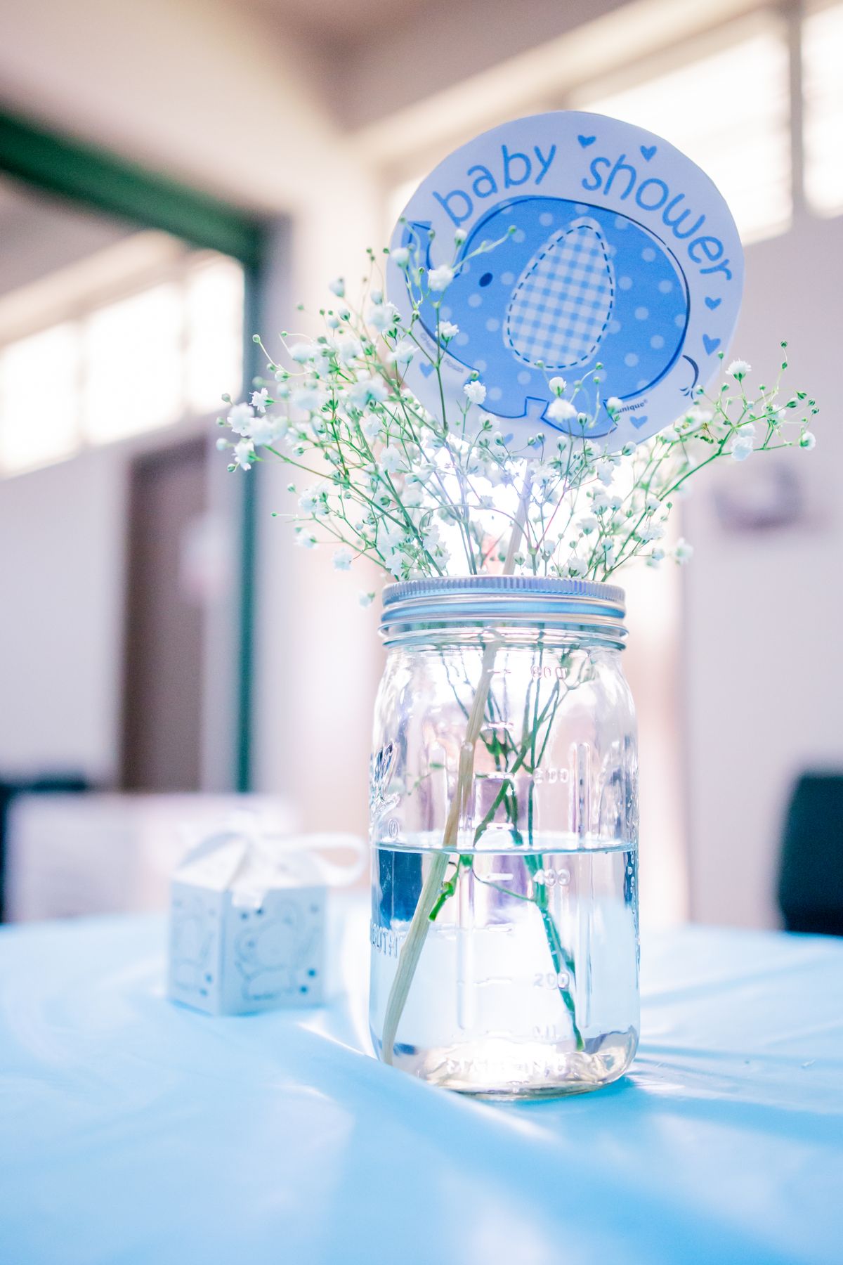 Mason jar with flowers and baby shower decoration on blue tablecloth, creating a serene ambiance. Stock Photo.