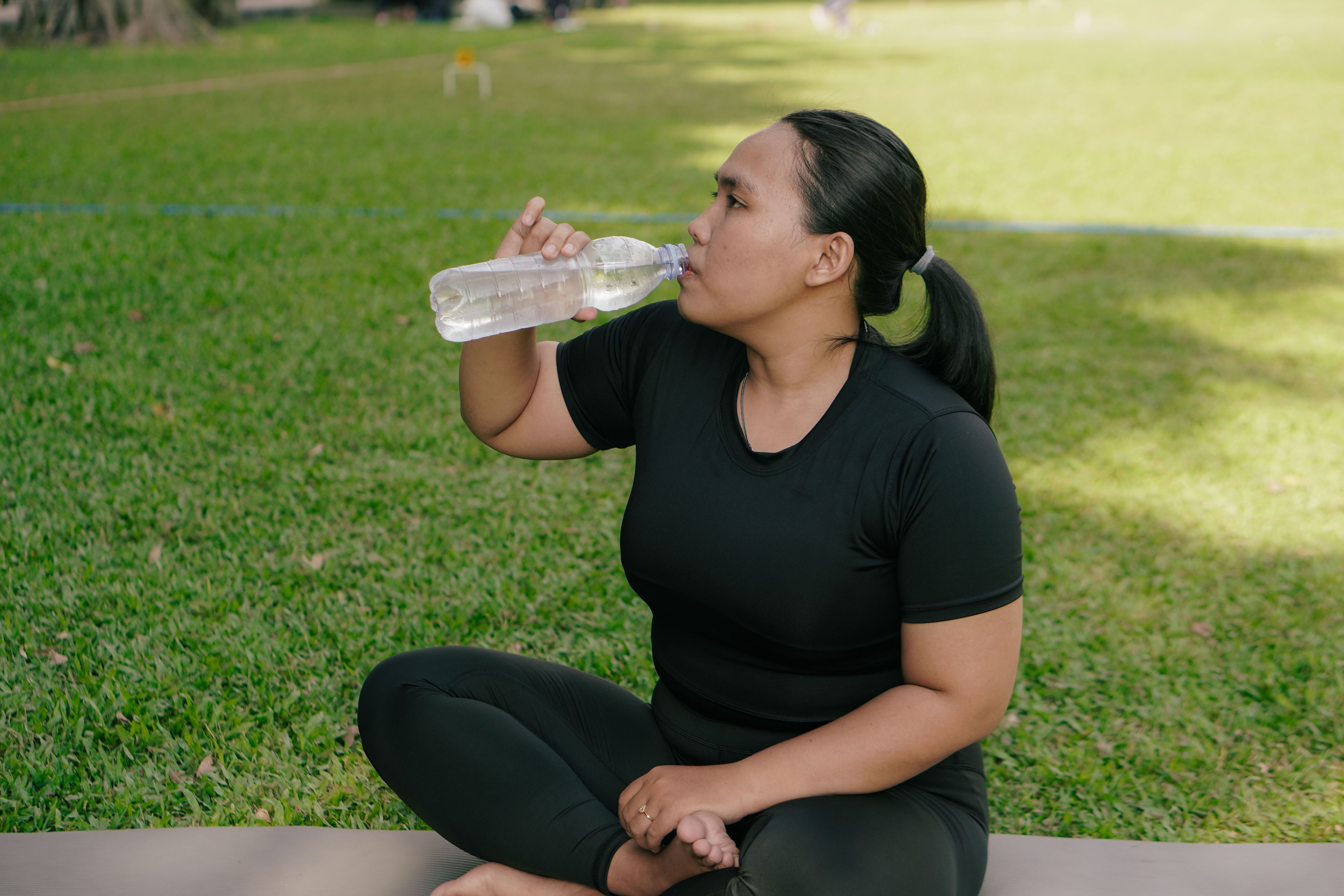 Woman drinking water post-workout in a park, promoting hydration and healthy lifestyle outdoors.