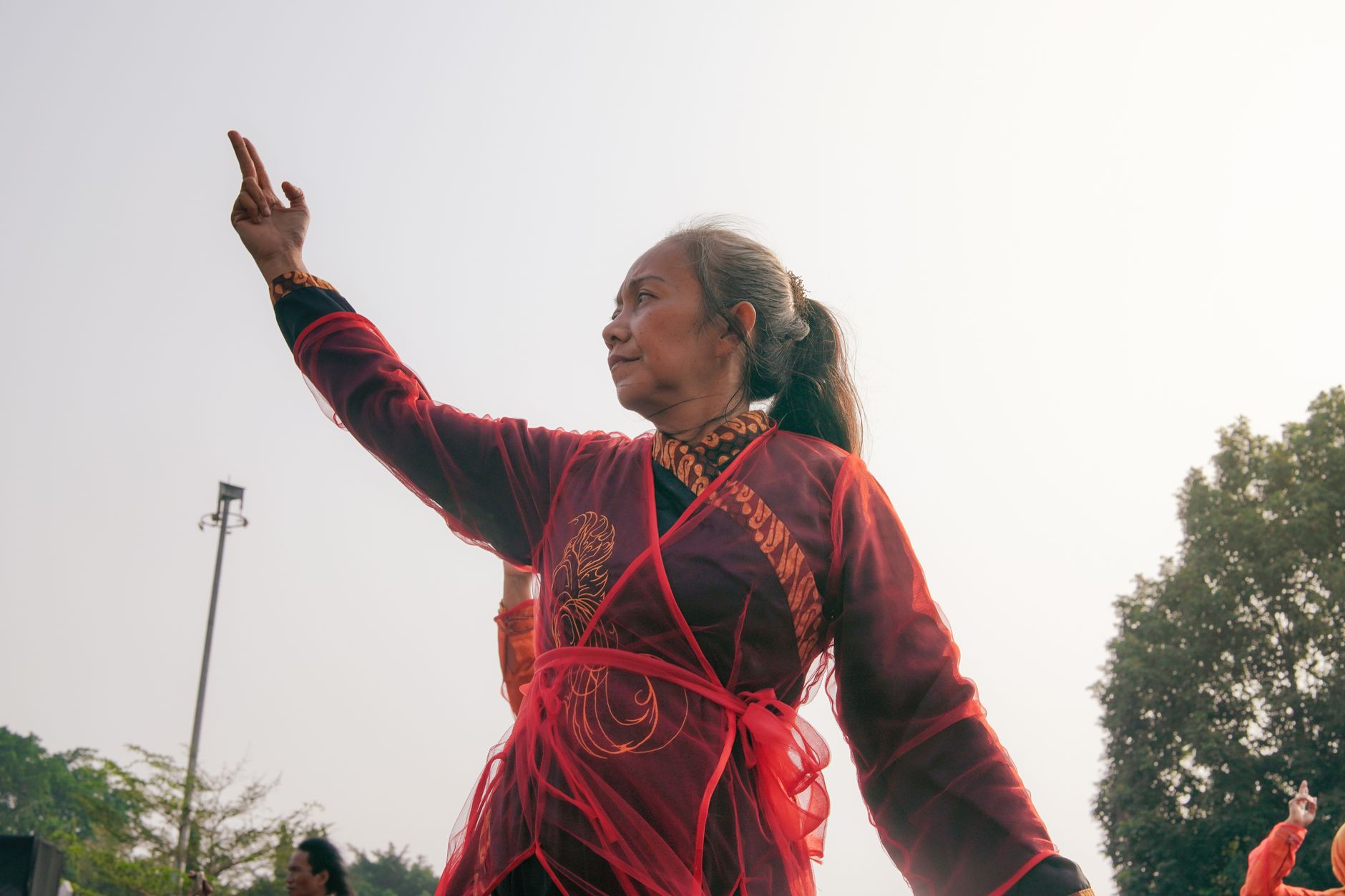 An elderly woman practicing Tai Chi in traditional attire during the day outdoors.