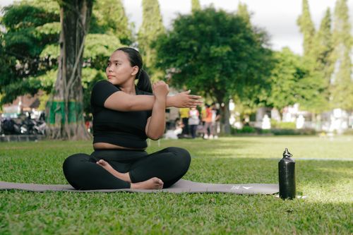 Free Woman in activewear stretching on a yoga mat outside on a sunny day, embracing a healthy lifestyle. Stock Photo