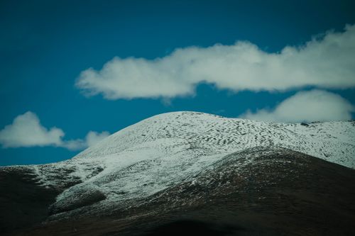 Free Captivating view of a snow-capped mountain with a clear blue sky and fluffy clouds, offering a serene natural landscape. Stock Photo