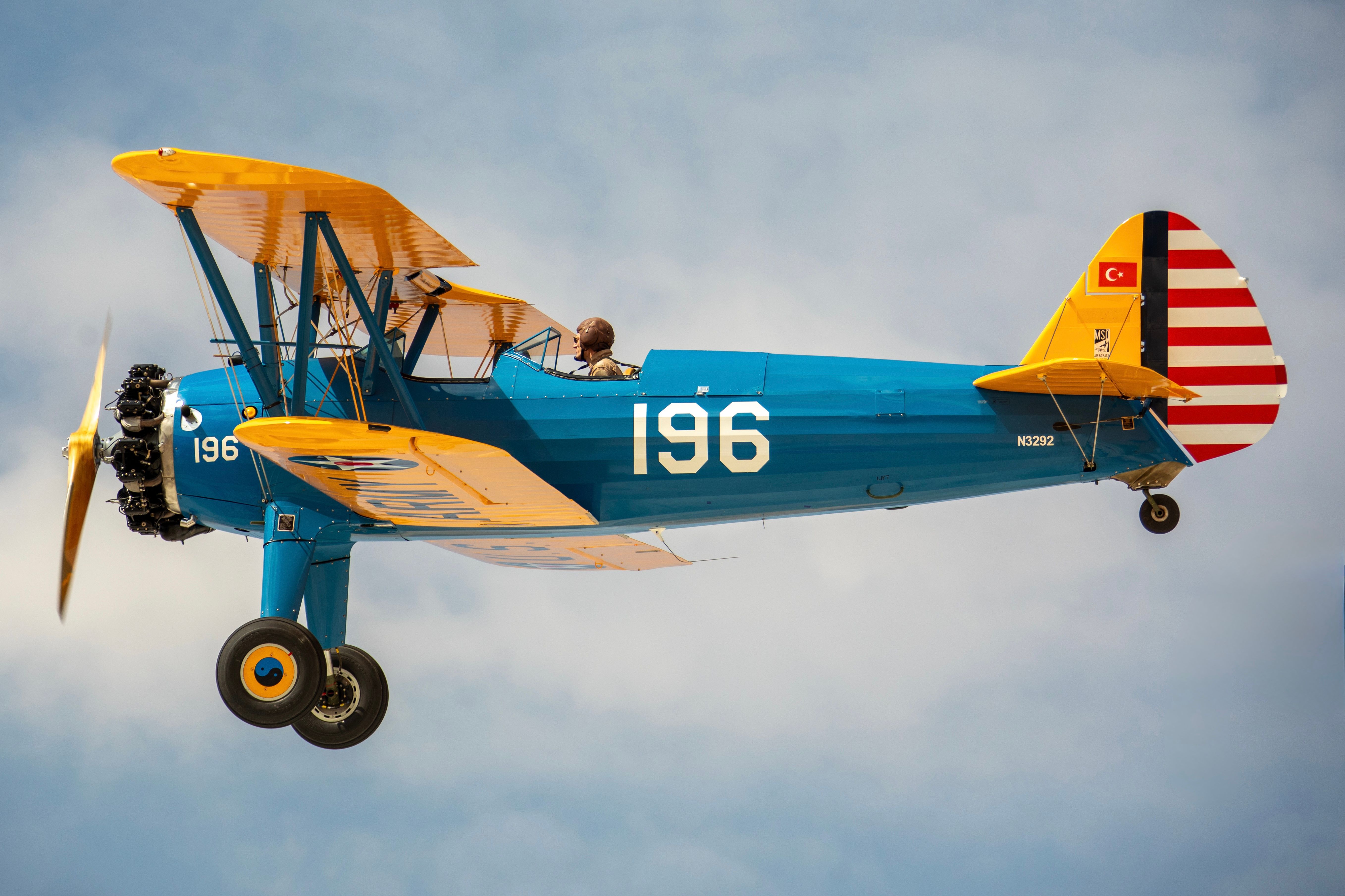 A classic blue and yellow biplane with a pilot flying against a clear sky, showcasing vintage aviation.