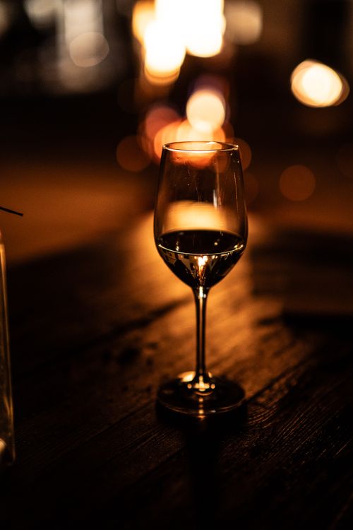 Free A wine glass elegantly illuminated against a warm bokeh background on a wooden table. Stock Photo