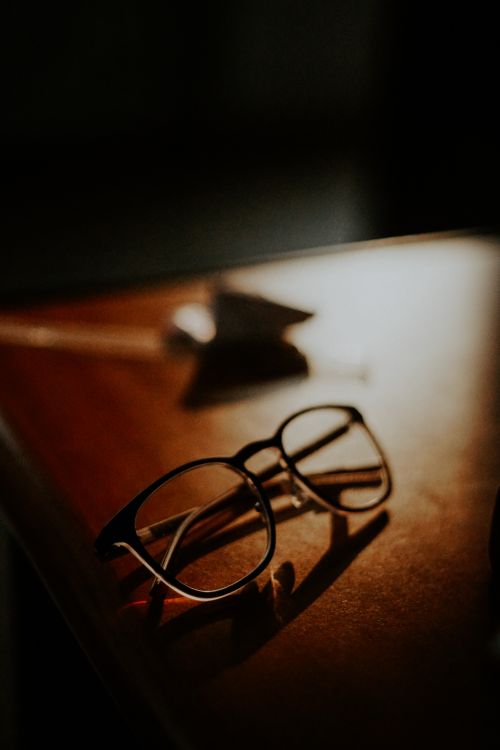 Free Aesthetic visual of eyeglasses resting on a wooden surface with dramatic lighting. Stock Photo