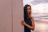 日落时分，一名女子拿着冲浪板站在海边