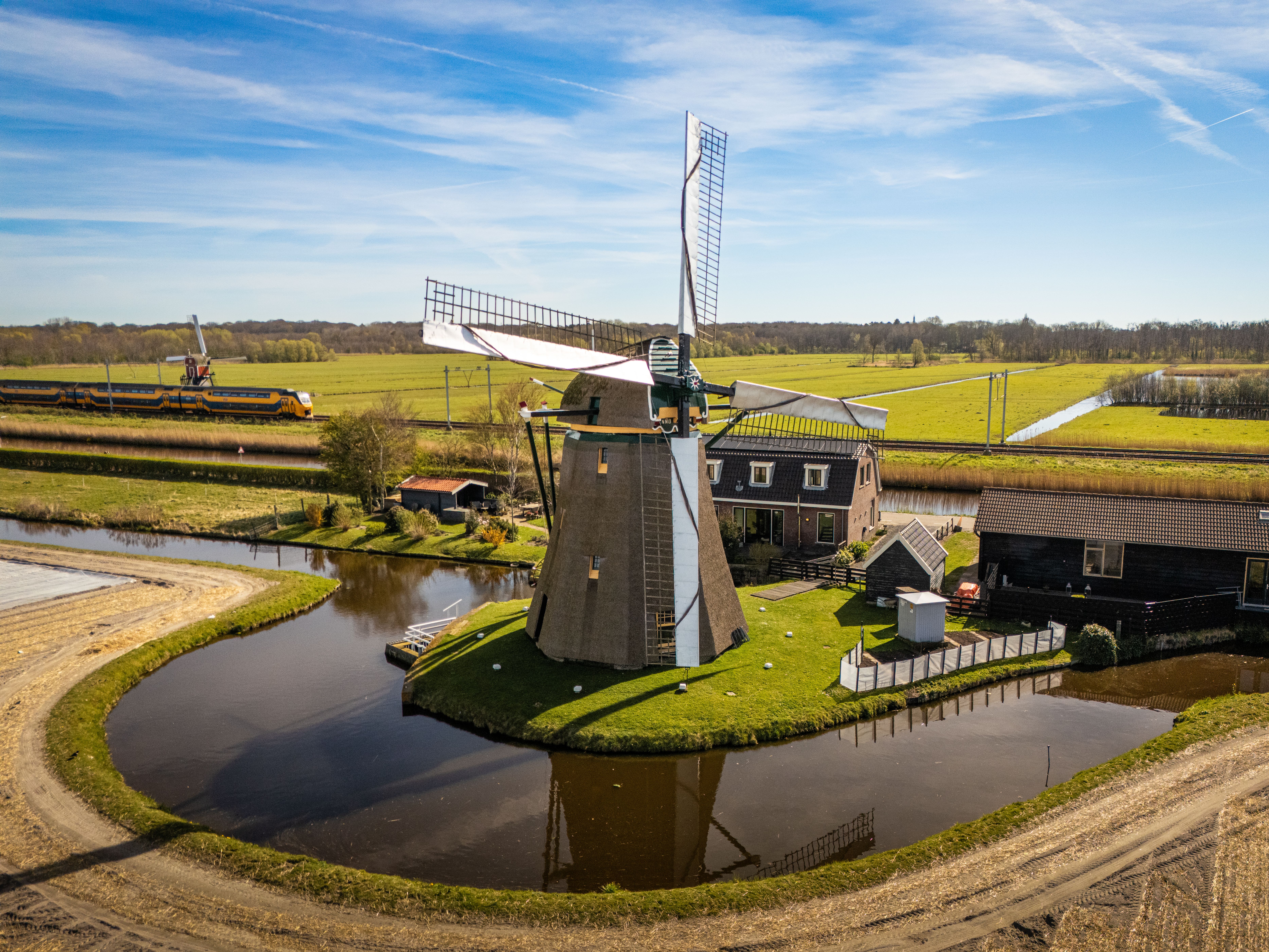 Historic Dutch windmill surrounded by greenery and a canal in Noordwijkerhout, Netherlands.