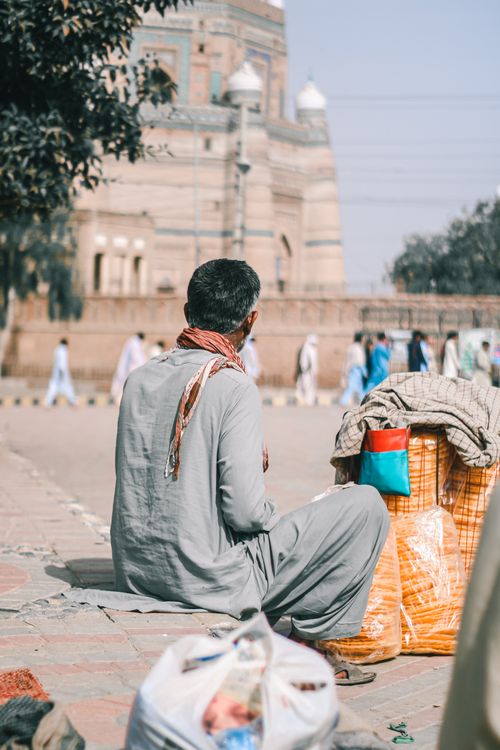 Free A man sits by his merchandise near a historic building in Multan, Pakistan. Stock Photo