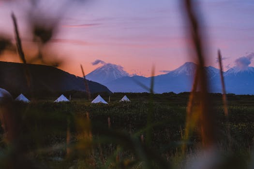 Campsite view in Kamchatka Krai with tents and snow-capped mountains during sunset. Ideal for nature and travel lovers.