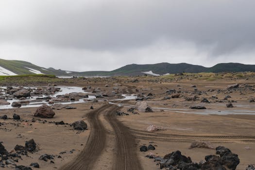 Explore the rocky terrain of Kamchatka Krai with winding dirt paths and a dramatic sky.