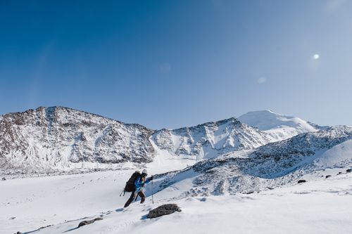 Free A lone hiker treks through a snow-covered mountain under a clear blue sky. Stock Photo