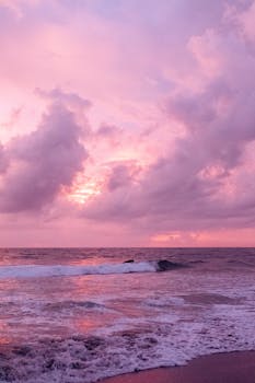 Captivating pink sunset sky over the ocean with gentle waves and dramatic clouds.