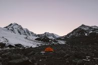 宁静的山地景观中，日落时分白雪皑皑的山峰与橙色帐篷相映，非常适合冒险主题