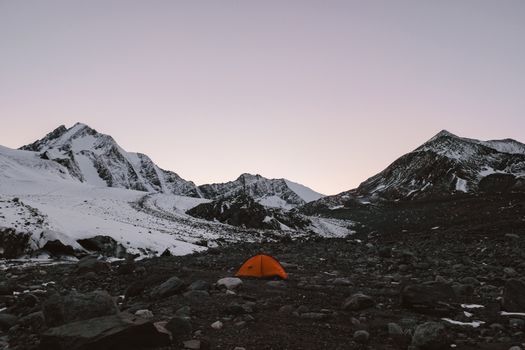 宁静的山地景观中，日落时分白雪皑皑的山峰与橙色帐篷相映，非常适合冒险主题