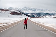一名穿着红色毛衣的女子指着空荡荡的道路，指向雄伟的雪山