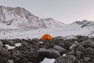 在布满岩石、白雪皑皑的山脉中，一顶橙色露营帐篷静静坐落，捕捉着宁静的自然风光