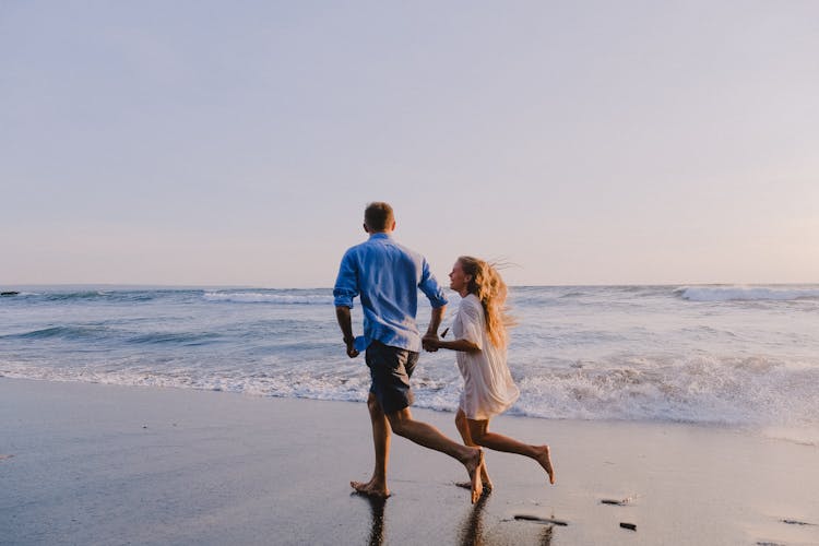 Couple Running Barefoot On Shore