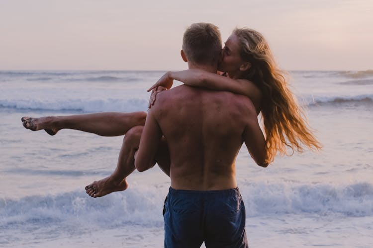 Back View Of A Man Carrying A Woman At The Beach