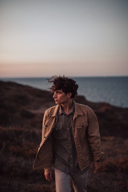 Free A young man walks along a coastal path at dusk, ocean backdrop creating a serene atmosphere. Stock Photo