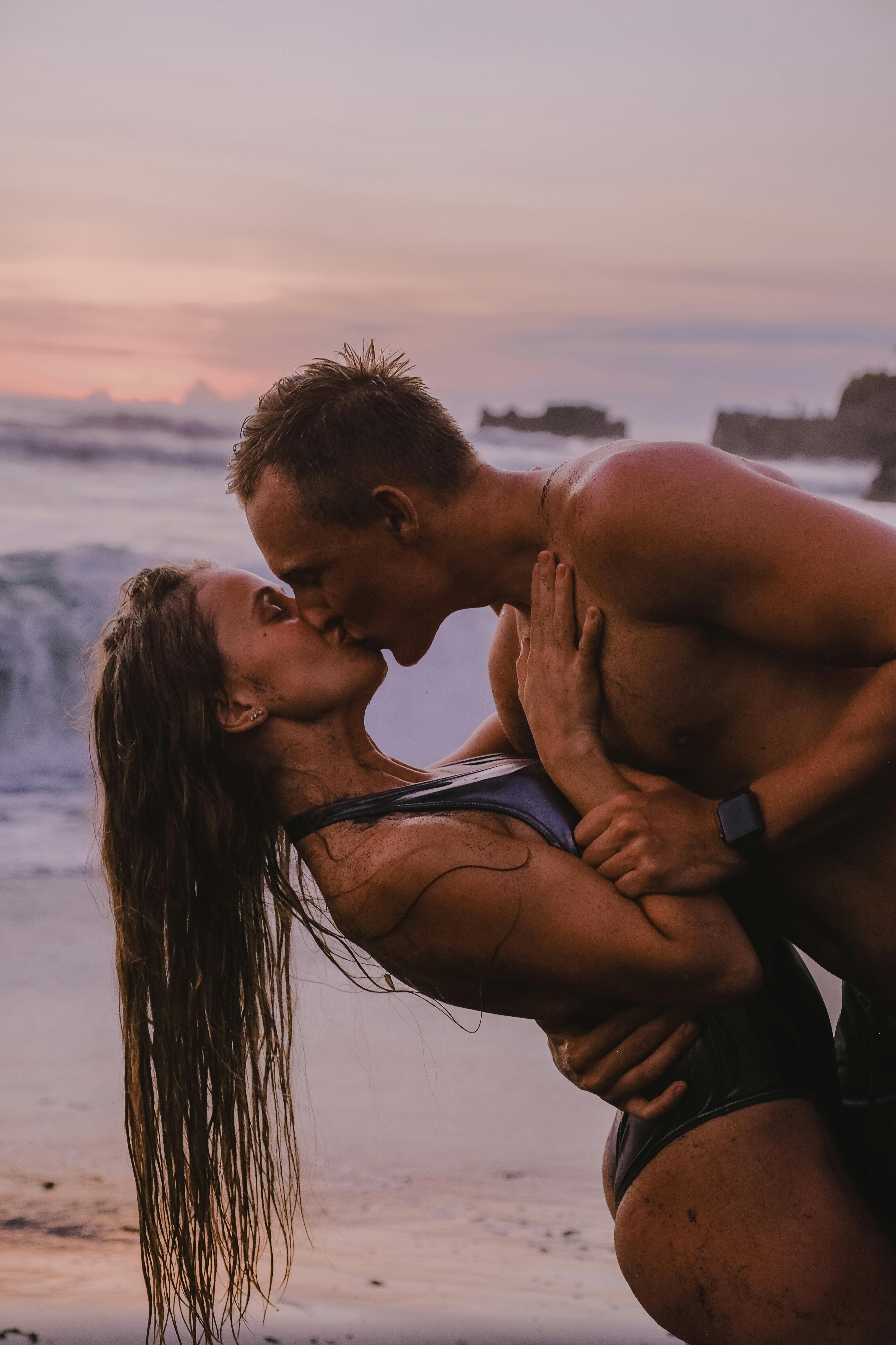 Couple sharing a passionate kiss on the beach during a vibrant sunset.