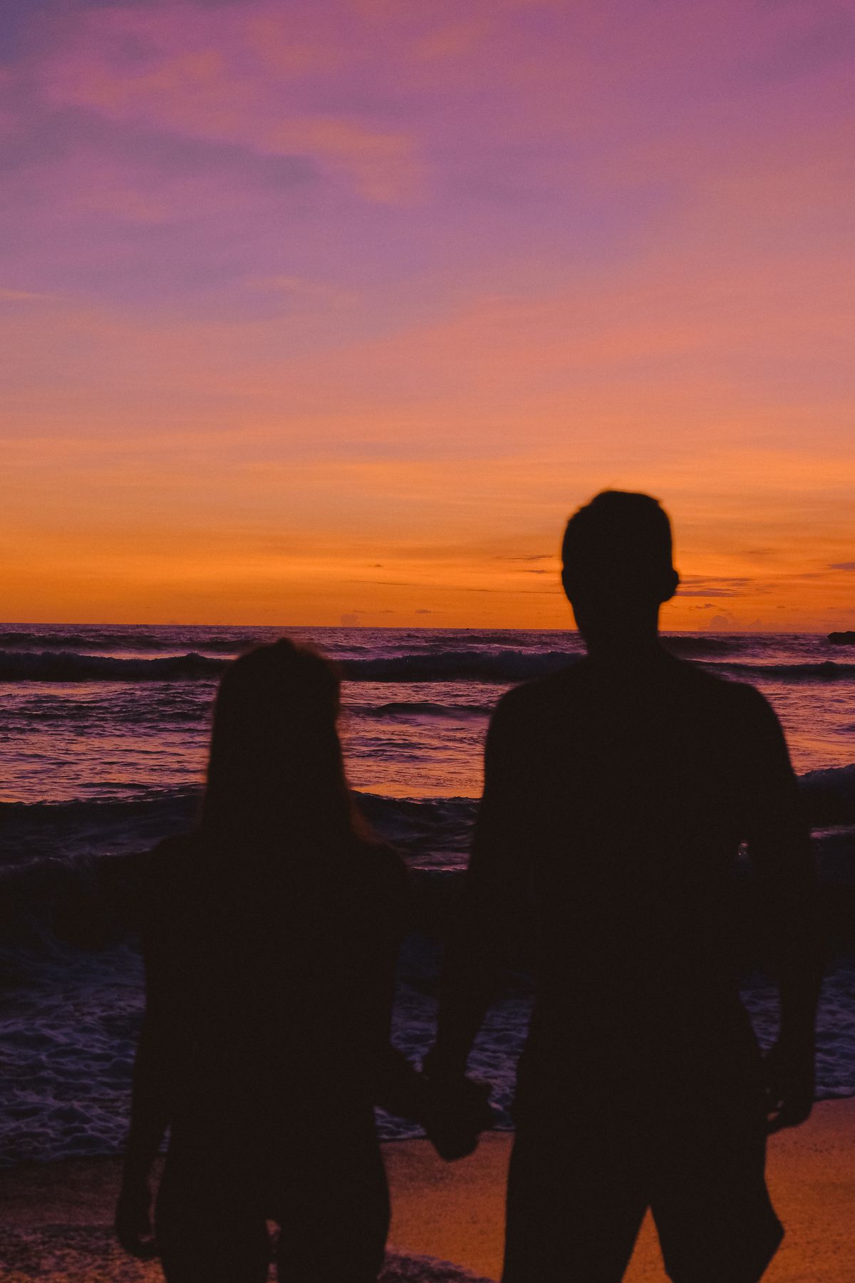 Deux silhouettes séparées face à la mer au coucher du soleil