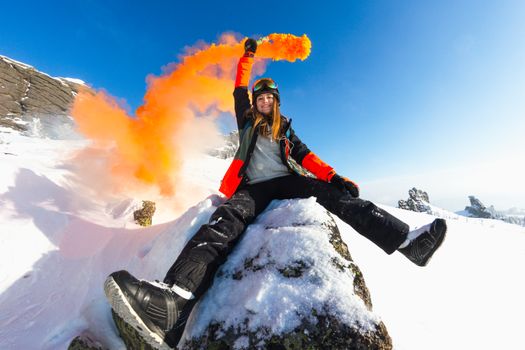 蓝天下，雪山中一位手持橙色烟雾弹的女人微笑着