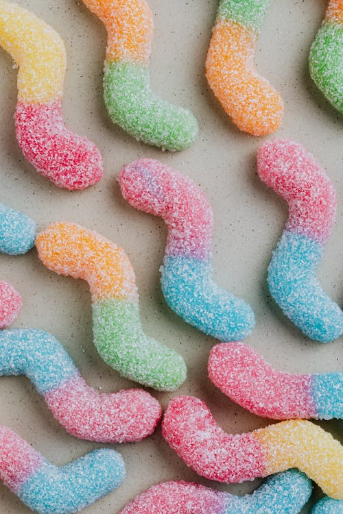 Top view of colorful sweet sugar gummy worms arranged on gray surface in candy store