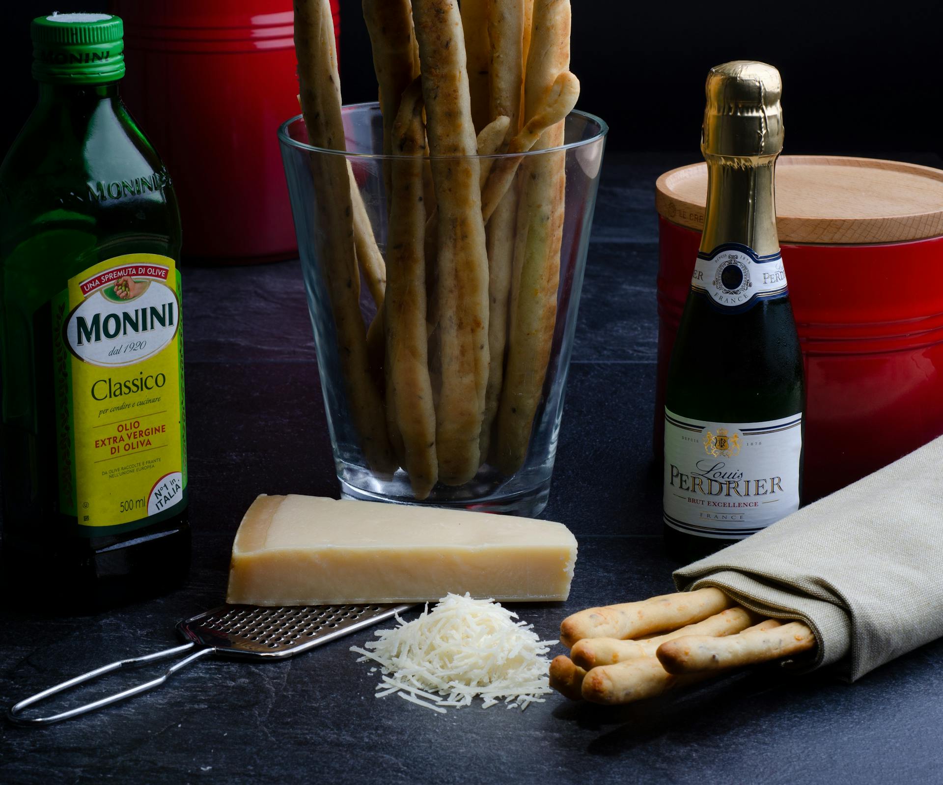 A dark and delicious Italian food composition featuring cheese, breadsticks, wine, and olive oil.