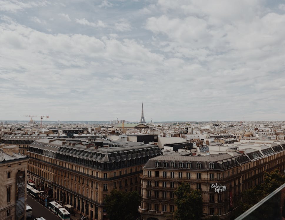 High angle of aged buildings of old Paris with Eiffel Tower at distance under cloudy sky