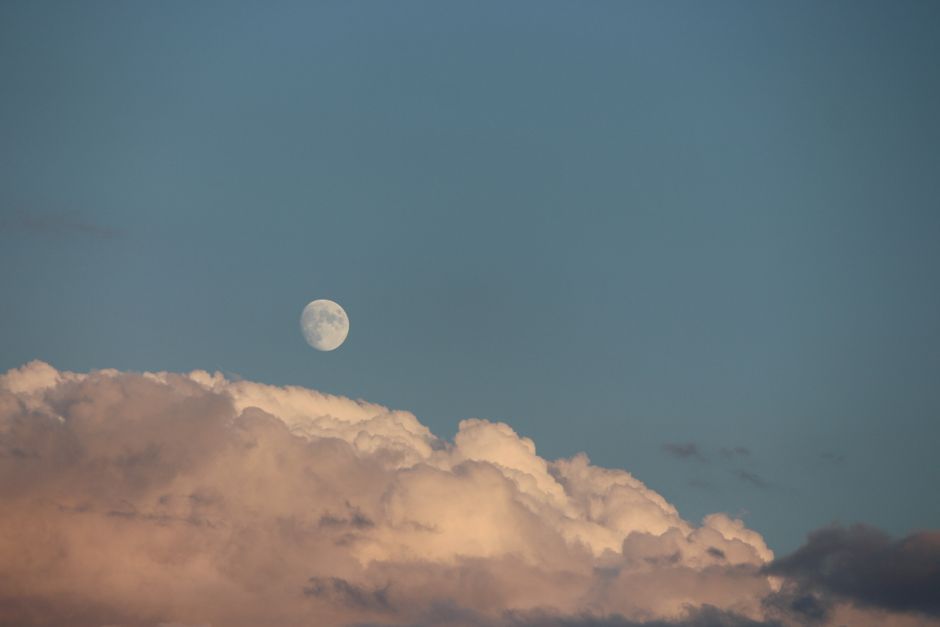 Tranquil image of the moon above colorful clouds on a clear evening sky.