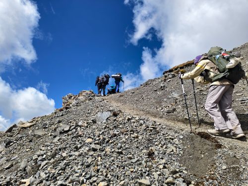 Free Group of hikers climbing a rocky mountain trail under a clear blue sky. Adventure and exploration theme. Stock Photo