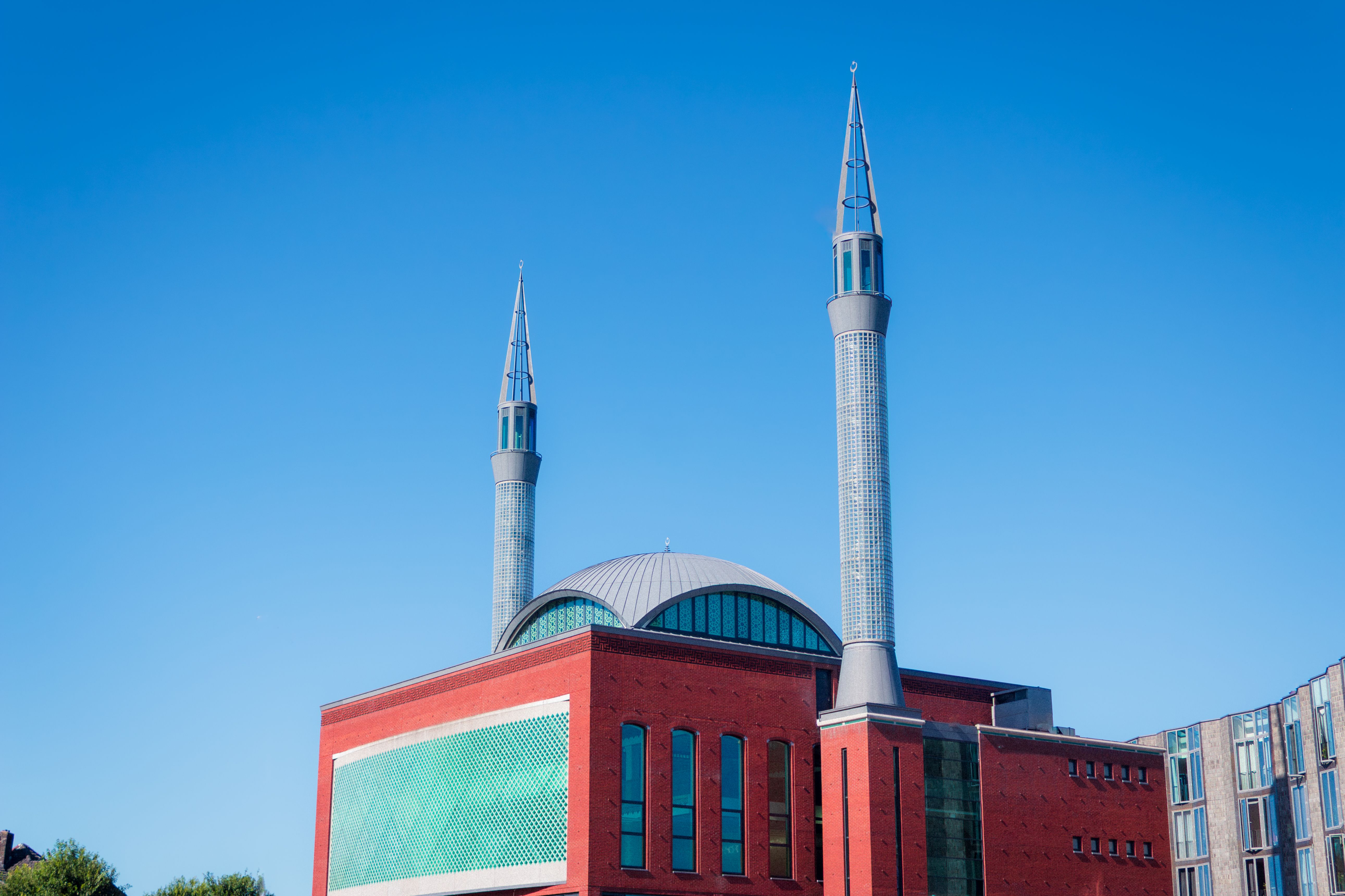 A contemporary mosque with sleek twin minarets stands against a bright blue sky, showcasing modern architectural design.