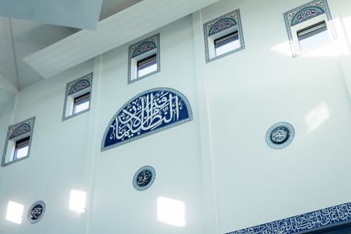 Free Interior view of mosque wall featuring traditional Arabic calligraphy and decorative windows. Stock Photo