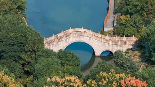 Free Aerial shot of an ancient stone bridge surrounded by lush greenery and a serene river. Stock Photo