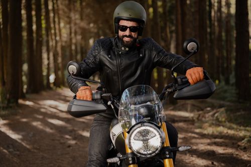 Free Bearded man in leather jacket on motorcycle enjoying a ride through the forest. Stock Photo