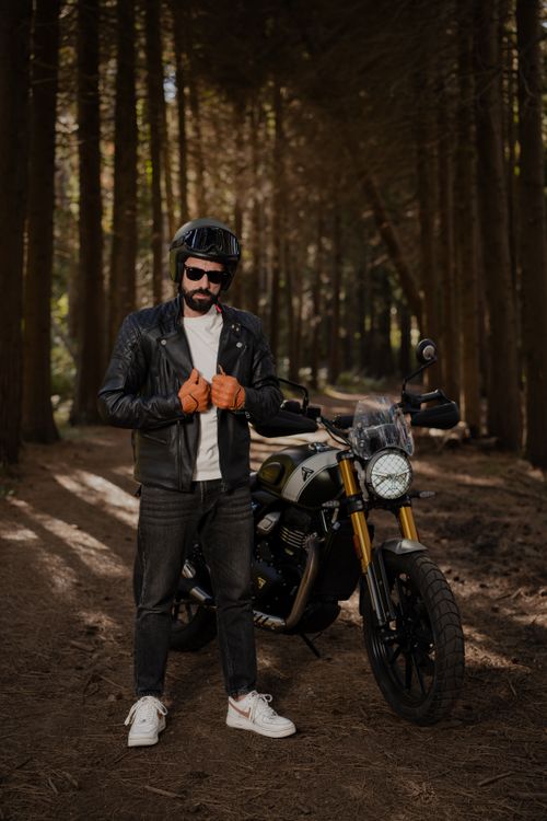 Free Motorcyclist in leather jacket standing near bike in wooded area, conveying adventure and freedom. Stock Photo