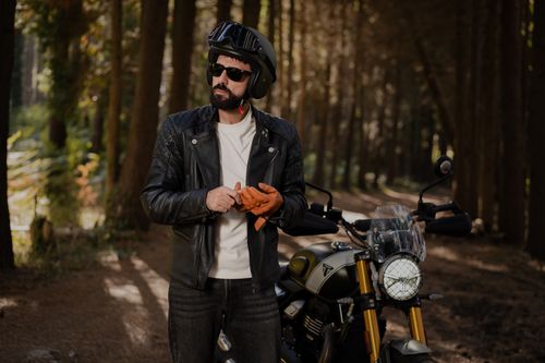 Free Man in leather jacket preparing to ride motorcycle in peaceful forest. Stock Photo