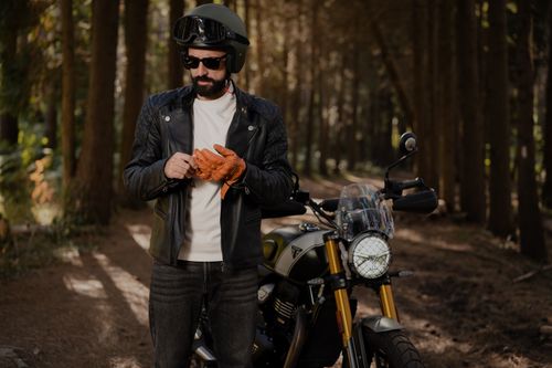 Free A fashionable biker in a leather jacket and helmet prepares his motorcycle for a ride through a forest trail. Stock Photo