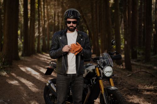 Free A biker in a leather jacket and helmet prepares for a ride in a serene forest setting. Stock Photo