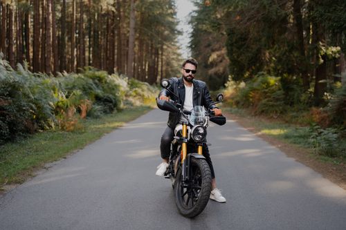 Free Man on motorcycle wearing leather jacket rides through a scenic forest road. Style and adventure captured in nature. Stock Photo