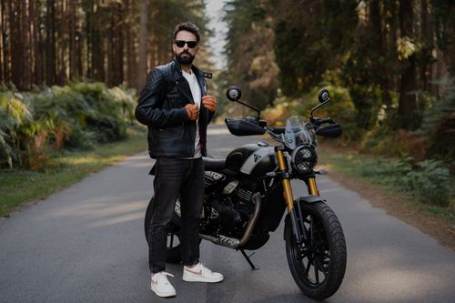 Free A man in a leather jacket stands beside a motorcycle on a forest road. Stock Photo