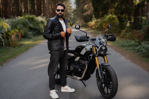 Free Stylish man posing with a motorcycle on a road surrounded by forest. Stock Photo