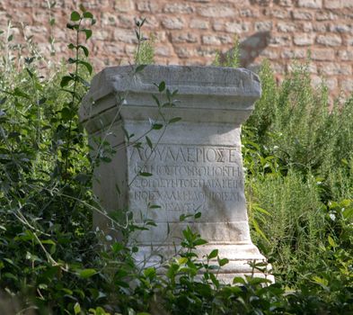 Ancient stone monument with Greek inscriptions surrounded by lush greenery, revealing historical ruins.