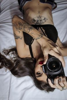 Top view of upside down woman with red lips lying on white bed with modern photo camera