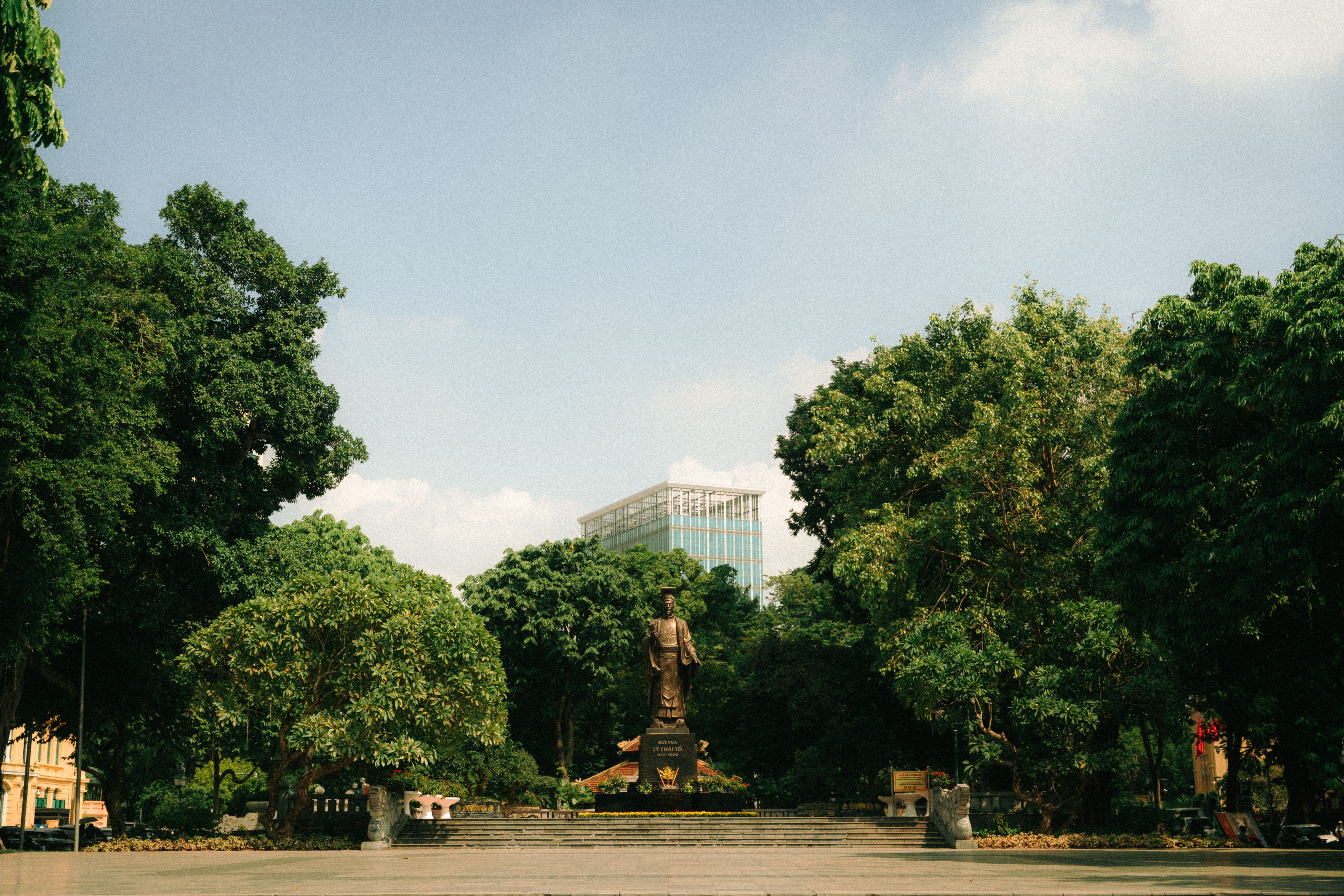 A statue amidst trees in an urban park with a glass building in the background.