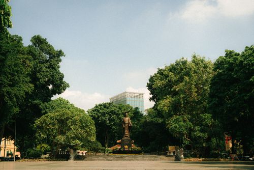 Free A statue amidst trees in an urban park with a glass building in the background. Stock Photo
