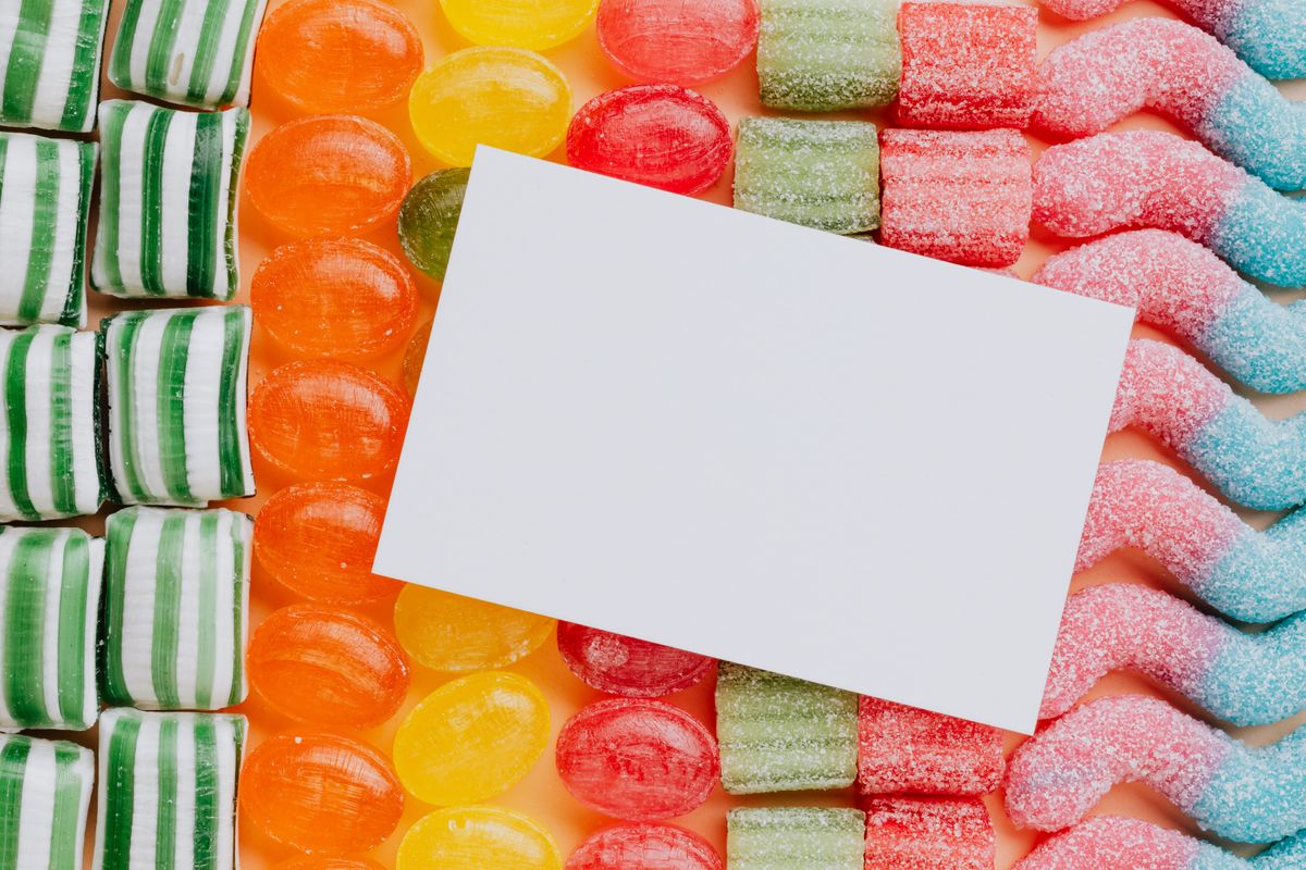 Closeup from above of white paper card composed on rows of delicious caramel gummy jelly sweets in modern candy shop